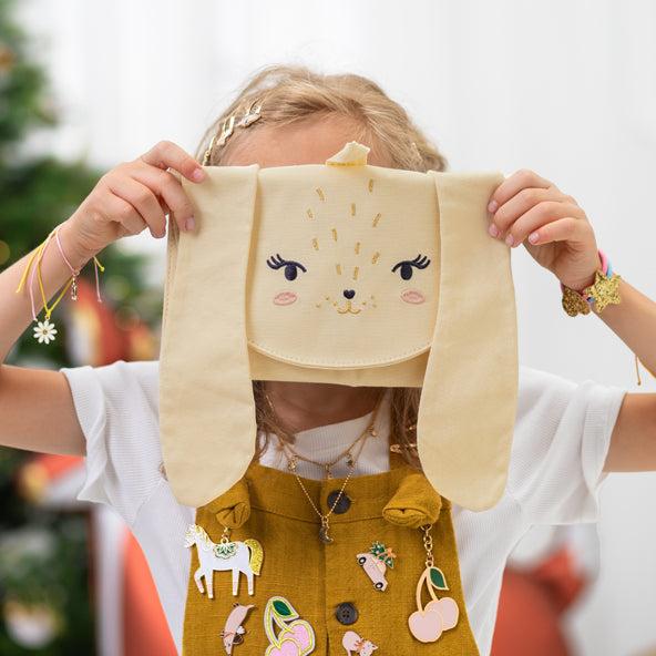 Kind houdt de opgevouwen konijnenadventskalender voor het gezicht en draagt kleurrijke sieraden en accessoires.