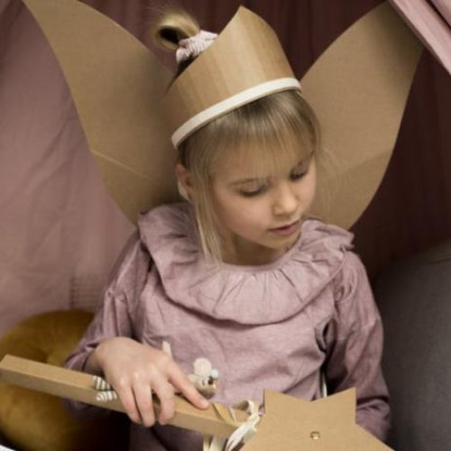 Kind met kartonnen tiara en feeënvleugels houdt een stervormige toverstaf op schoot.