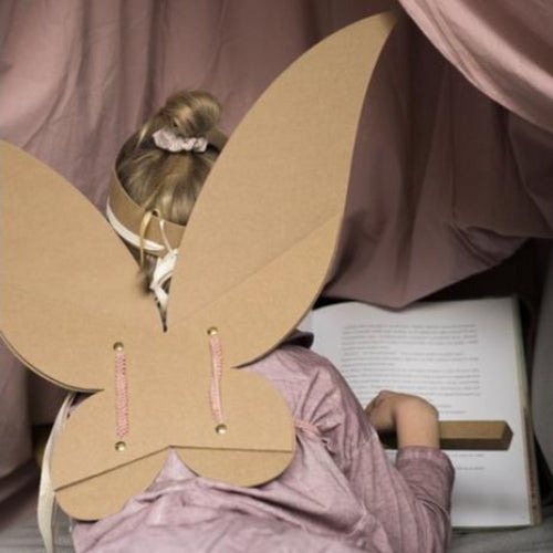 Kind van achteren met bruine kartonnen feeënvleugels en een tiara, zittend voor een open boek.