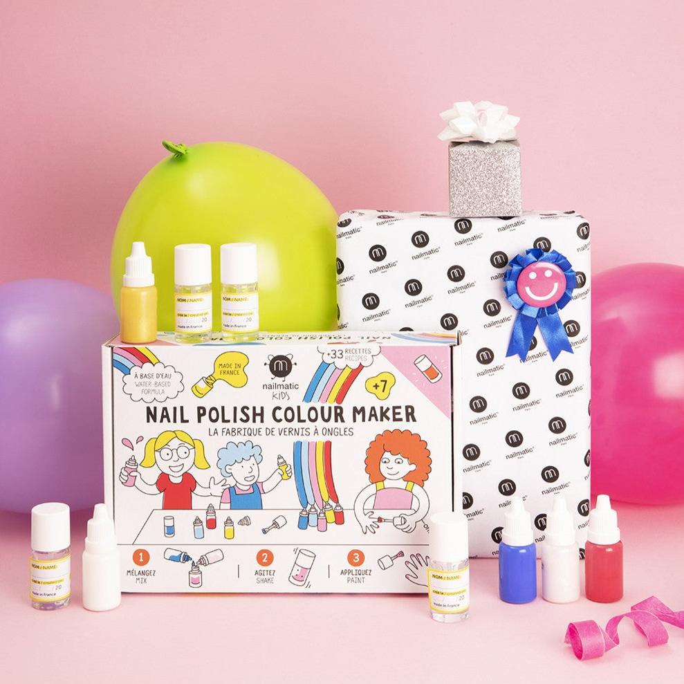 Nailmatic DIY-nagellakset met flesjes, ingepakte cadeaus en ballonnen op een roze achtergrond.