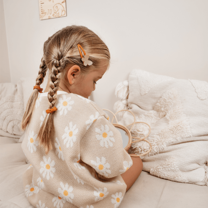 Meisje van achteren met twee vlechten en een oranje haarspeldje met een beige vlinder in haar haar.