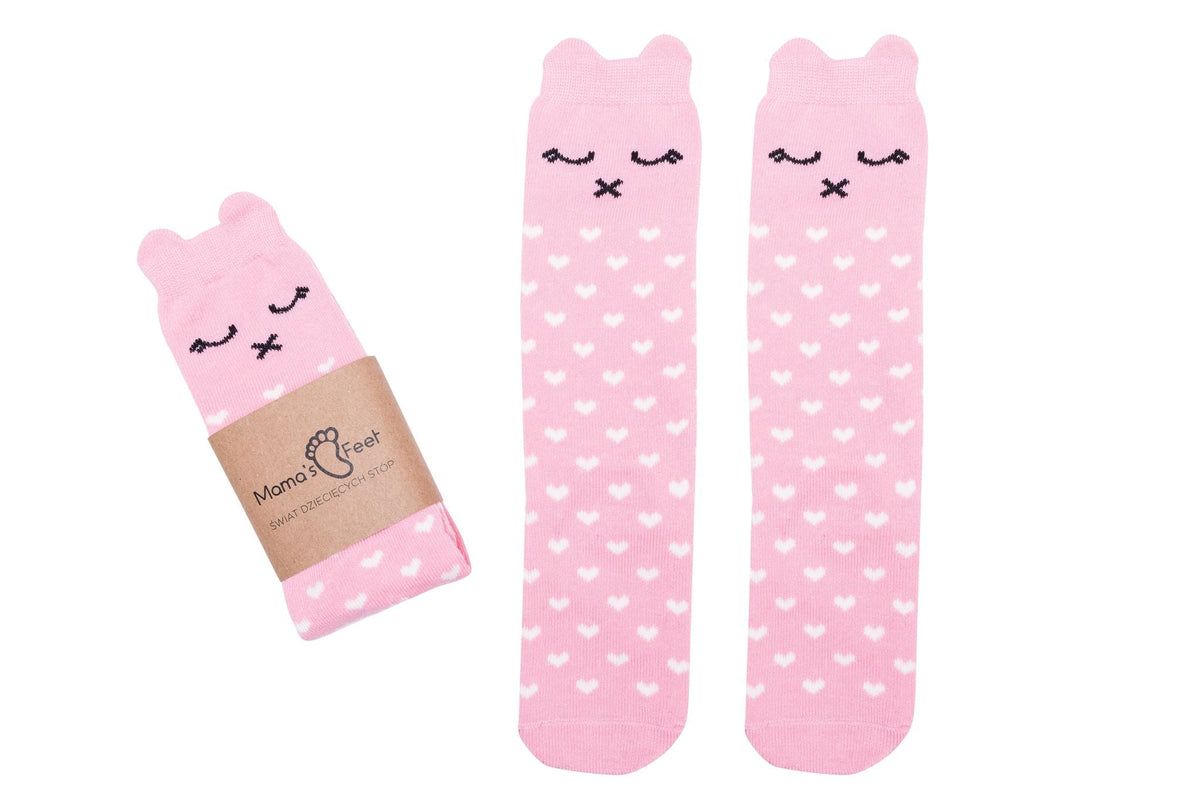 Roze Lilly a Pinky Kitty kniekousen met kattenoortjes en witte hartjes, naast een opgevouwen paar met wikkel.