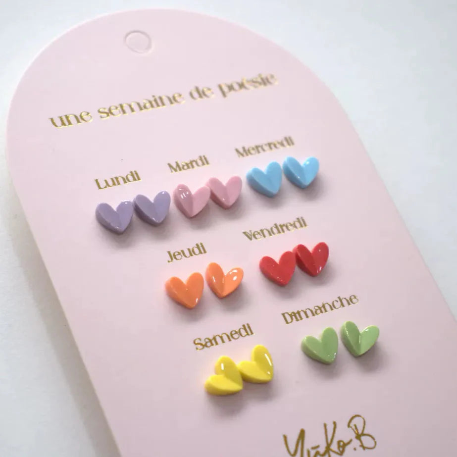 Roze kaart met zeven paar hartjesoorbellen in paars, roze, blauw, oranje, rood, geel en groen, schuin gefotografeerd.