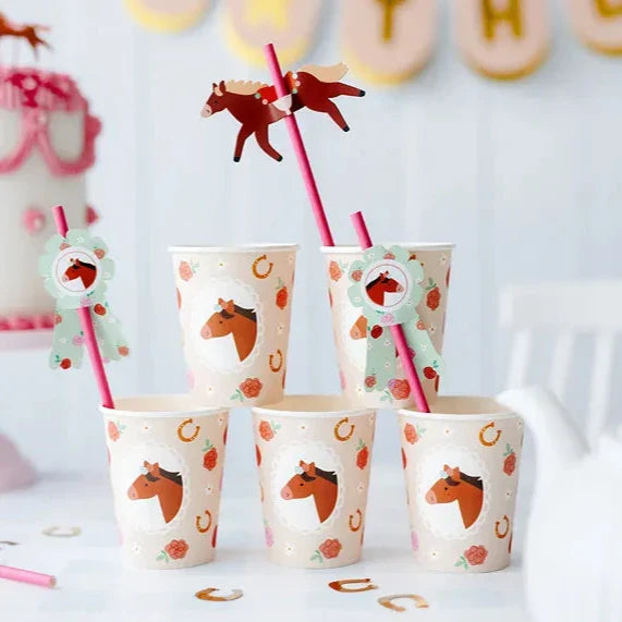 Roze rietjes met paard en mintgroene paardenrozetten in feestbekers met paardenprint op een gedekte tafel.