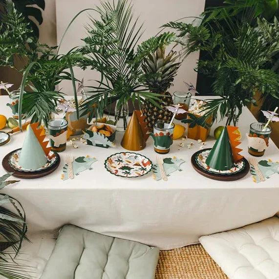 Groene servetten in dinosaurusvorm op een feesttafel met dinobordjes, feesthoedjes en tropische planten