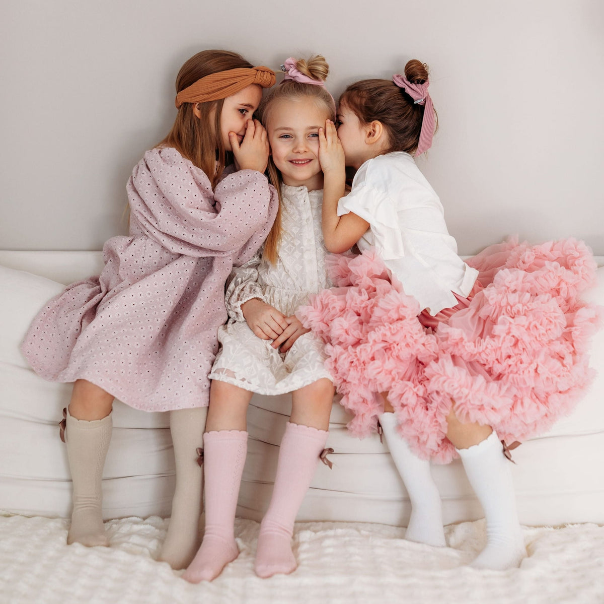 Drie meisjes op een bank met Josephine kniekousen in beige, roze en wit, met strikjes aan de zijkant.