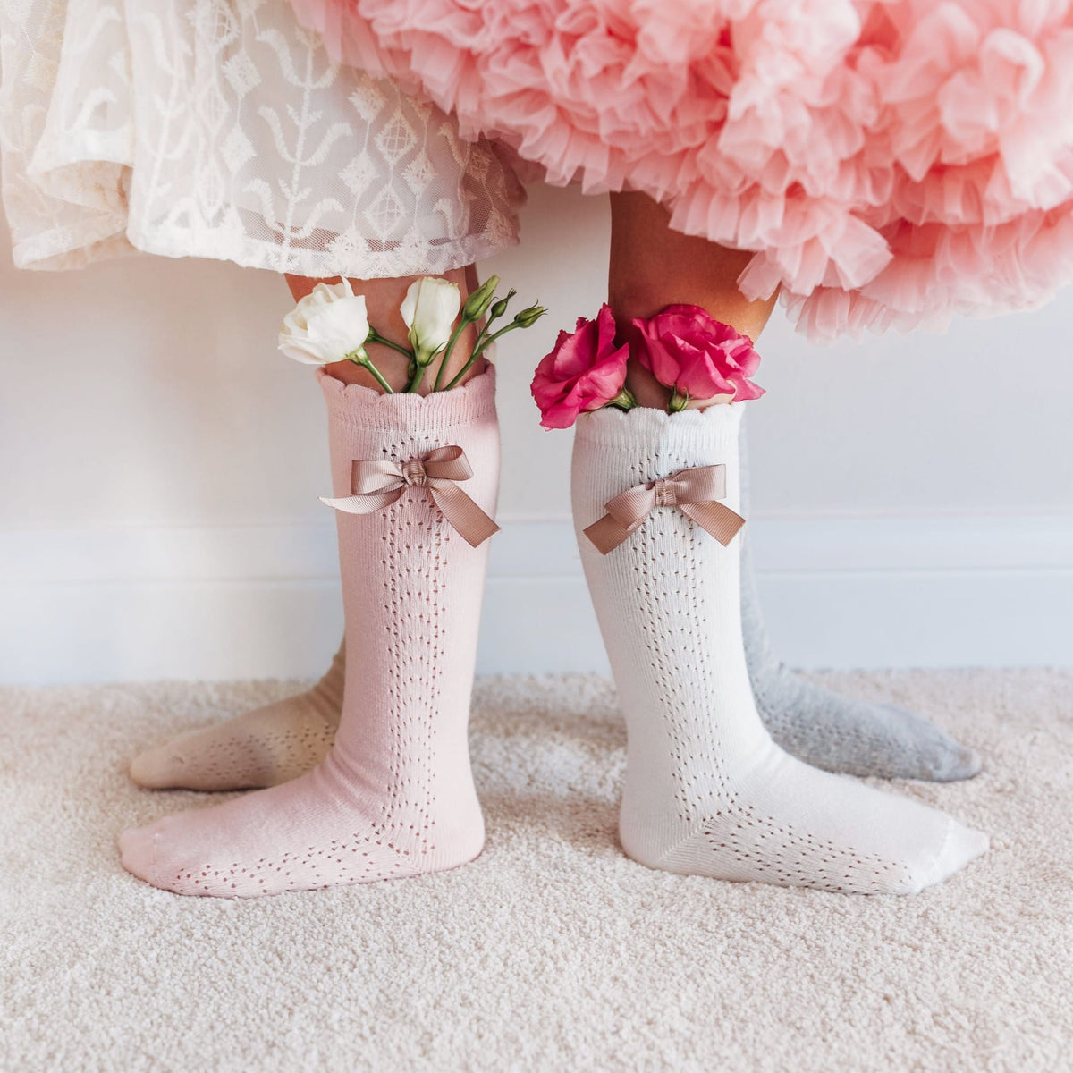 Roze, witte en grijze kniekousen met strikjes, gedragen door kinderen, met bloemen in de boorden.