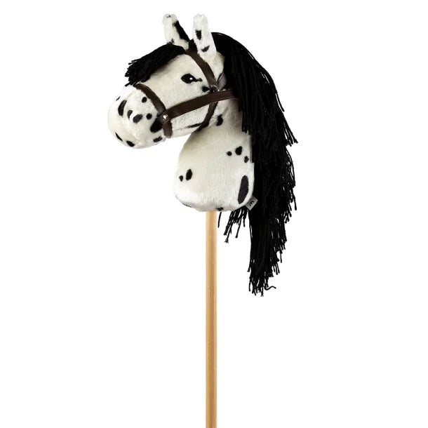 Wit stokpaardje met zwarte stippen, lange zwarte manen en een bruin hoofdstel, van opzij gezien.