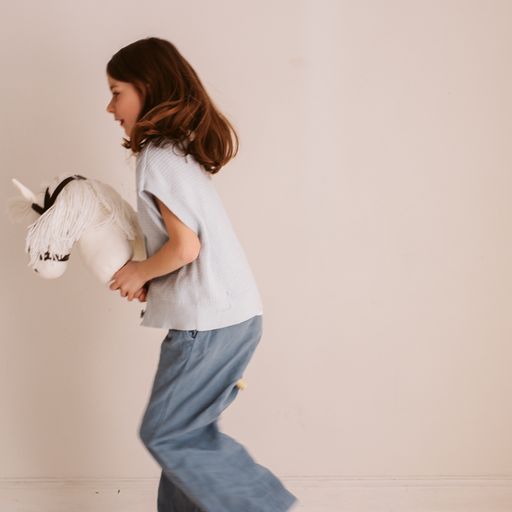 Kind speelt met een wit stokpaardje met lange witte manen en een bruin hoofdstel.