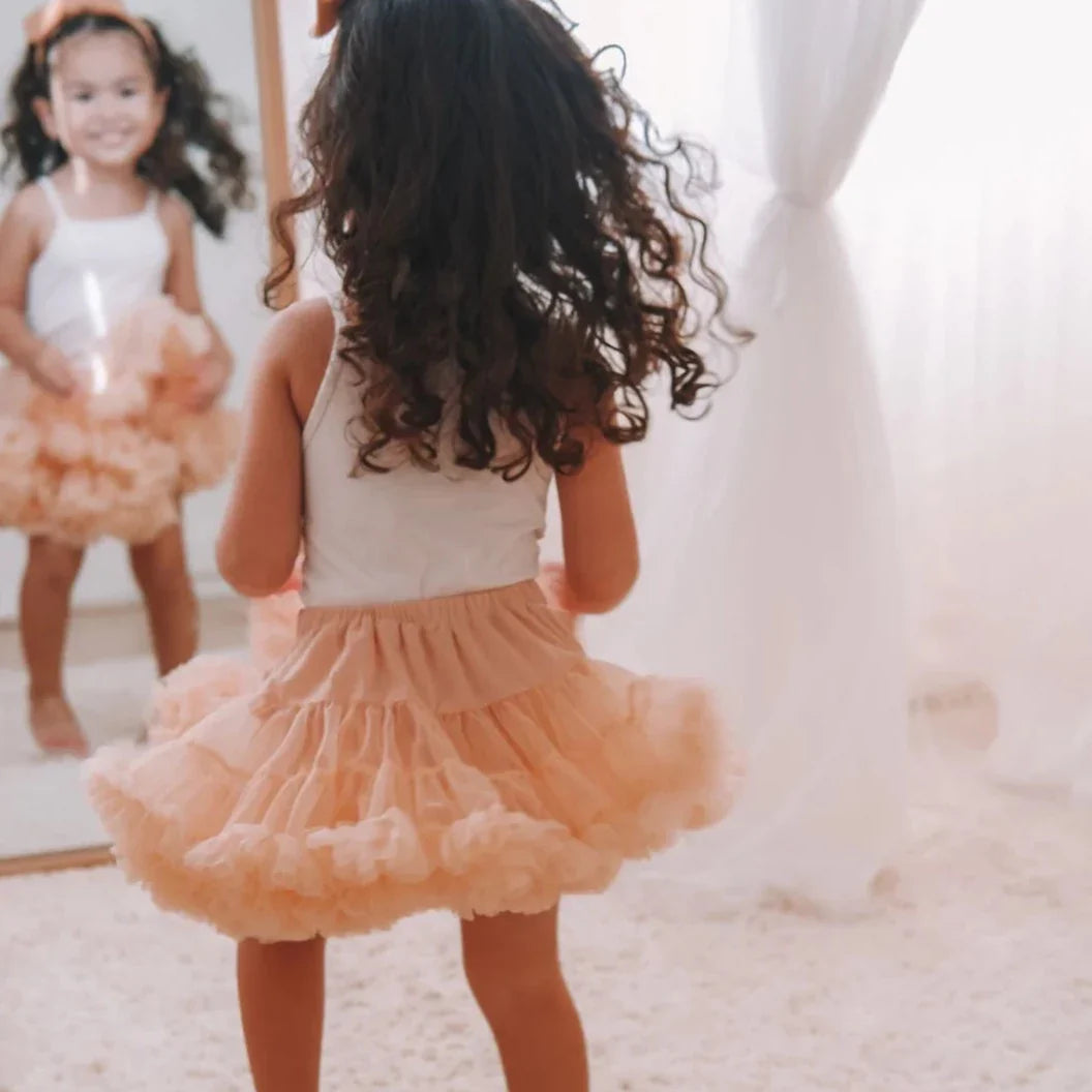 Achteraanzicht van een meisje in de perzikkleurige Loli tutu rok en een witte top voor een spiegel.