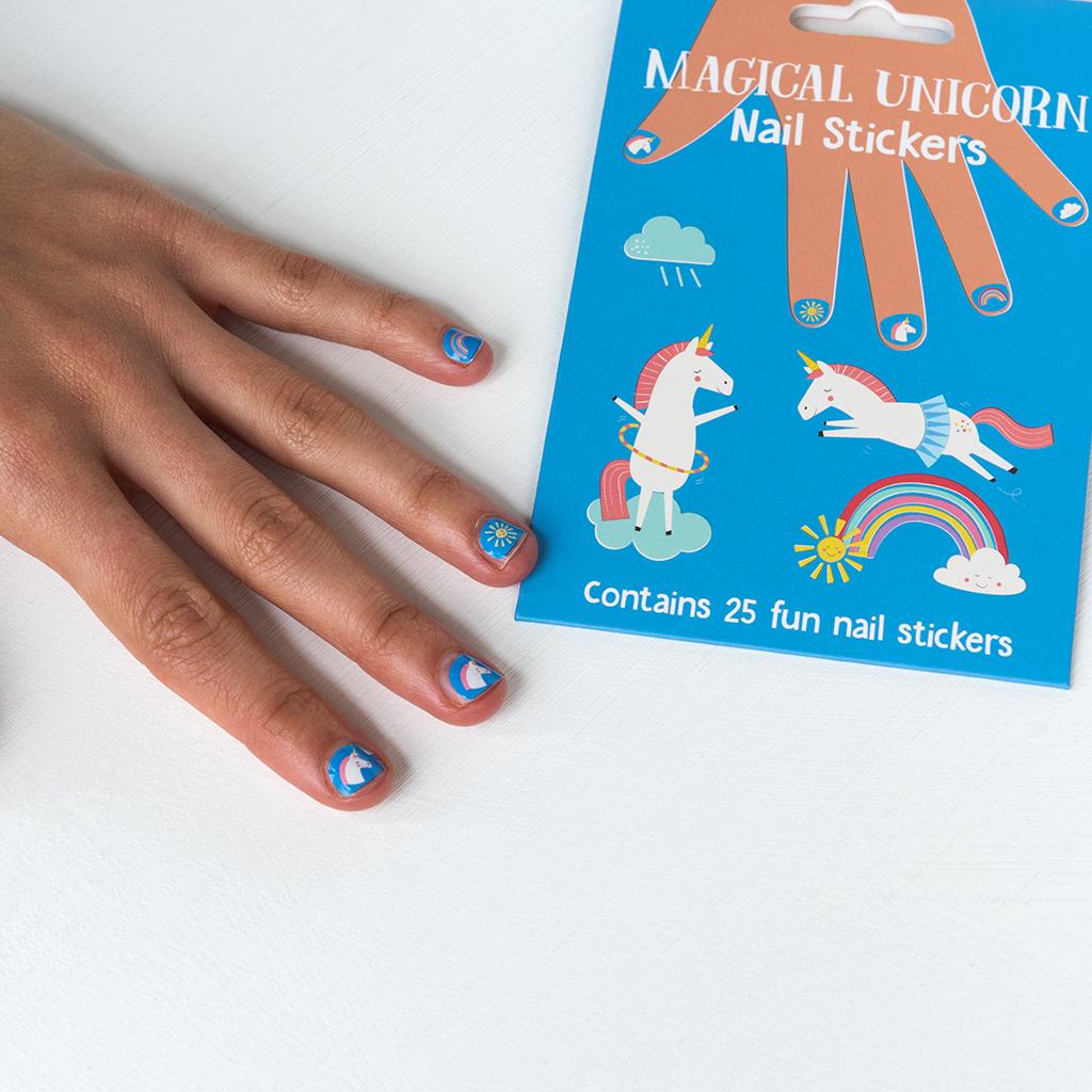 Hand met blauwe nagelstickers met eenhoorns, een regenboog en een zon naast de verpakking.