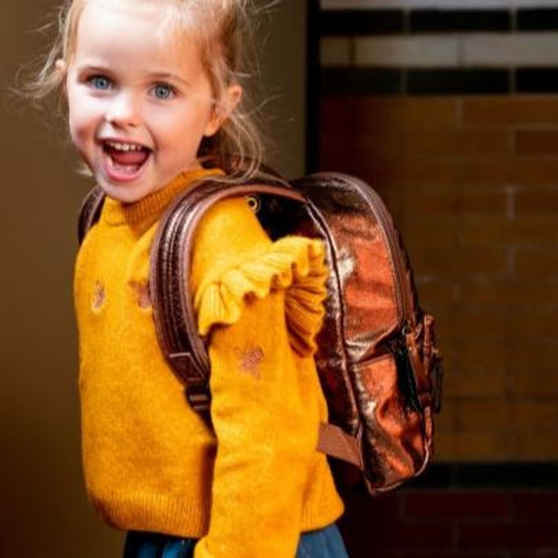 Zijaanzicht van een kind met gele trui dat de glanzende Walker rugtas in Dark Gold draagt.