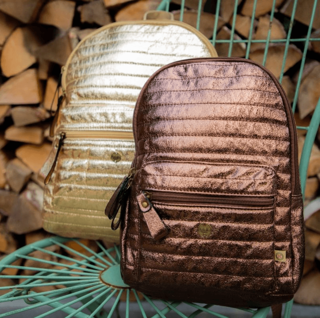 Walker rugtas in Dark Gold met voorvak met rits, naast een lichtgouden rugtas op een groene stoel.