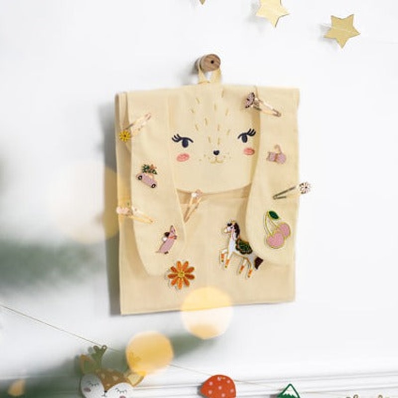 Crèmekleurige konijnenadventskalender aan de muur, versierd met haaraccessoires en sleutelhangers.