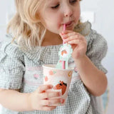 Kind drinkt met een roze rietje uit een kartonnen beker met paardenprint, bloemen en hoefijzers.