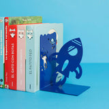 Blauwe boekensteun in raketvorm naast een rij kinderboeken op een blauwe ondergrond.