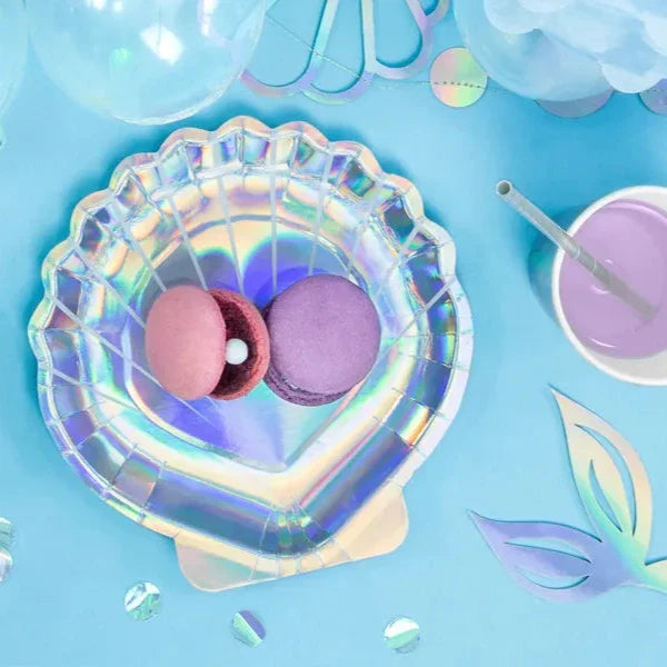 Glanzend zeeschelpvormig bordje met roze en paarse macarons op een blauw gedekte feesttafel.