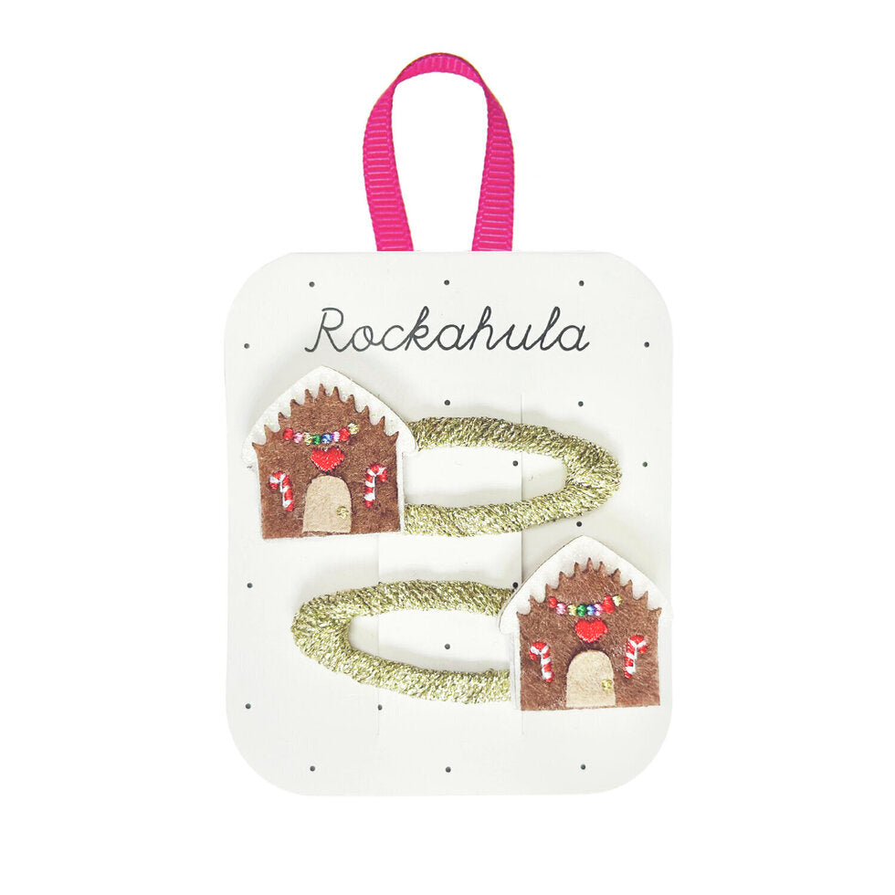 Twee goudkleurige haarclips met bruine peperkoekhuisjes, witte glitterdaken en kleurrijke geborduurde details.