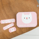 Roze Cookie The Cat-pleisterblikje met drie roze kattenpleisters ernaast op een houten tafel.