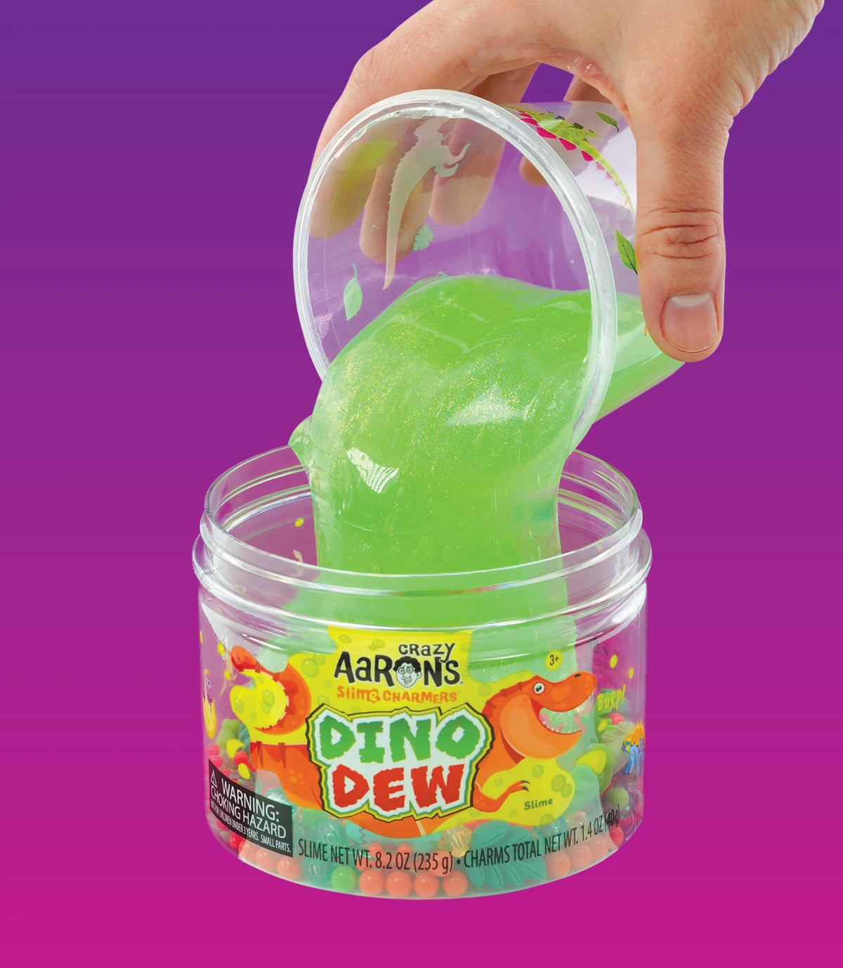 Een hand giet felgroen Crazy Aaron's Dino Dew slijm uit een doorzichtig bakje in de open pot.