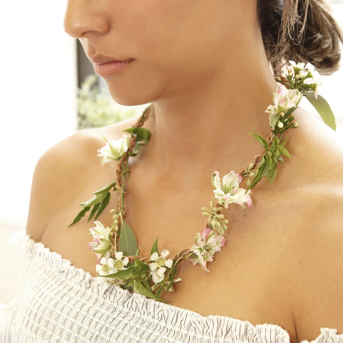 Detail van een bloemenketting met witte en lichtroze bloemen en groene bladeren, gedragen rond de hals.
