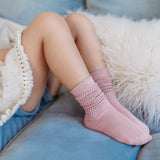 Kind met roze Dream Socks Pink sokken met structuurpatroon aan de enkels, zittend op een blauwe bank.