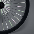 Fietswiel met Sparkle-spaakreflectoren in lichtgroen, roze en wit tegen een grijze achtergrond.