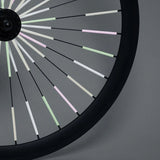 Fietswiel met Sparkle-spaakreflectoren in lichtgroen, roze en wit tegen een grijze achtergrond.