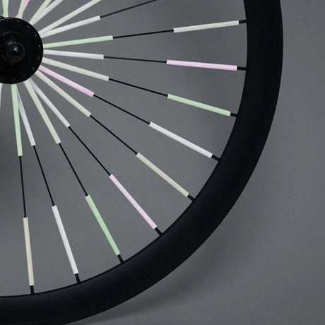 Fietswiel met Sparkle-spaakreflectoren in lichtgroen, roze en wit tegen een grijze achtergrond.