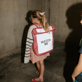Kind met een roze Flashbag Lou-rugzak met oplichtend reflecterend voorpaneel in een betonnen doorgang.
