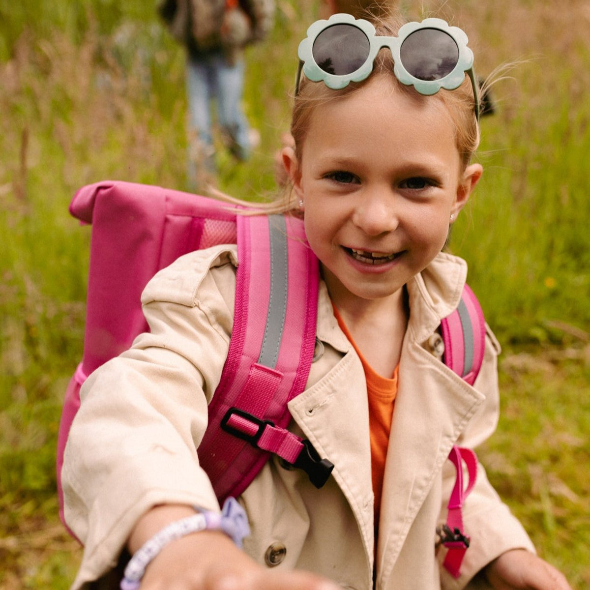 Kind draagt de roze Flashbag Lou-rugzak buiten, met reflecterende stroken op de schouderbanden en een borstclip.