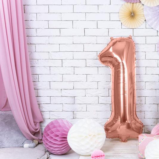 Roségouden folieballon 1 bij een witte bakstenen muur met roze gordijn en papieren feestdecoratie