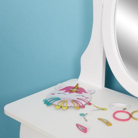 Eenhoornkaartje met kleurrijke haarclips op een witte kaptafel naast een spiegel en haarelastiekjes.