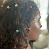 Roze, gele en blauwe haarparels in het krullende haar van een kind met glitter op de wang