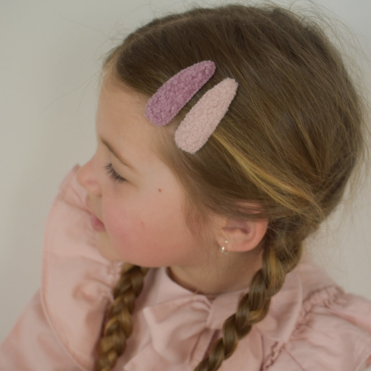 Meisje met twee haarspeldjes in beige en oudroze teddystof naast elkaar in haar gevlochten haar.