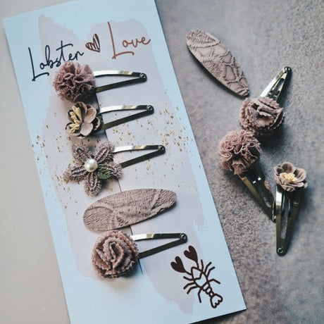 Haarspeldjes Misty Mauve met bloemen en ovale vormen in mauve tinten, op een kaartje en een grijze ondergrond.