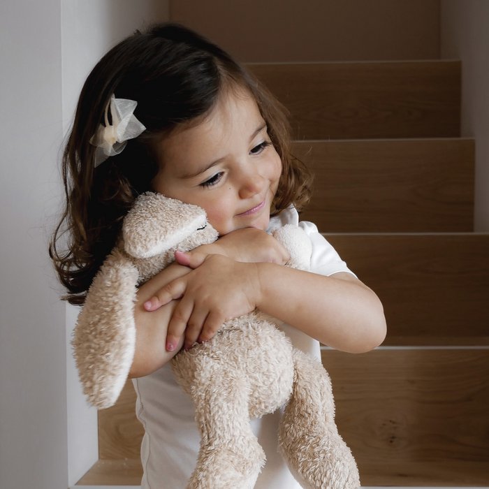 Kind met een crèmekleurig haarspeldje met organza strik knuffelt een pluchen konijn op de trap.