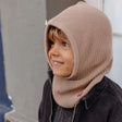 Kind met beige gebreide Hoody Latte van Hello Hossy over het hoofd en rond de hals, boven een donkere jas.