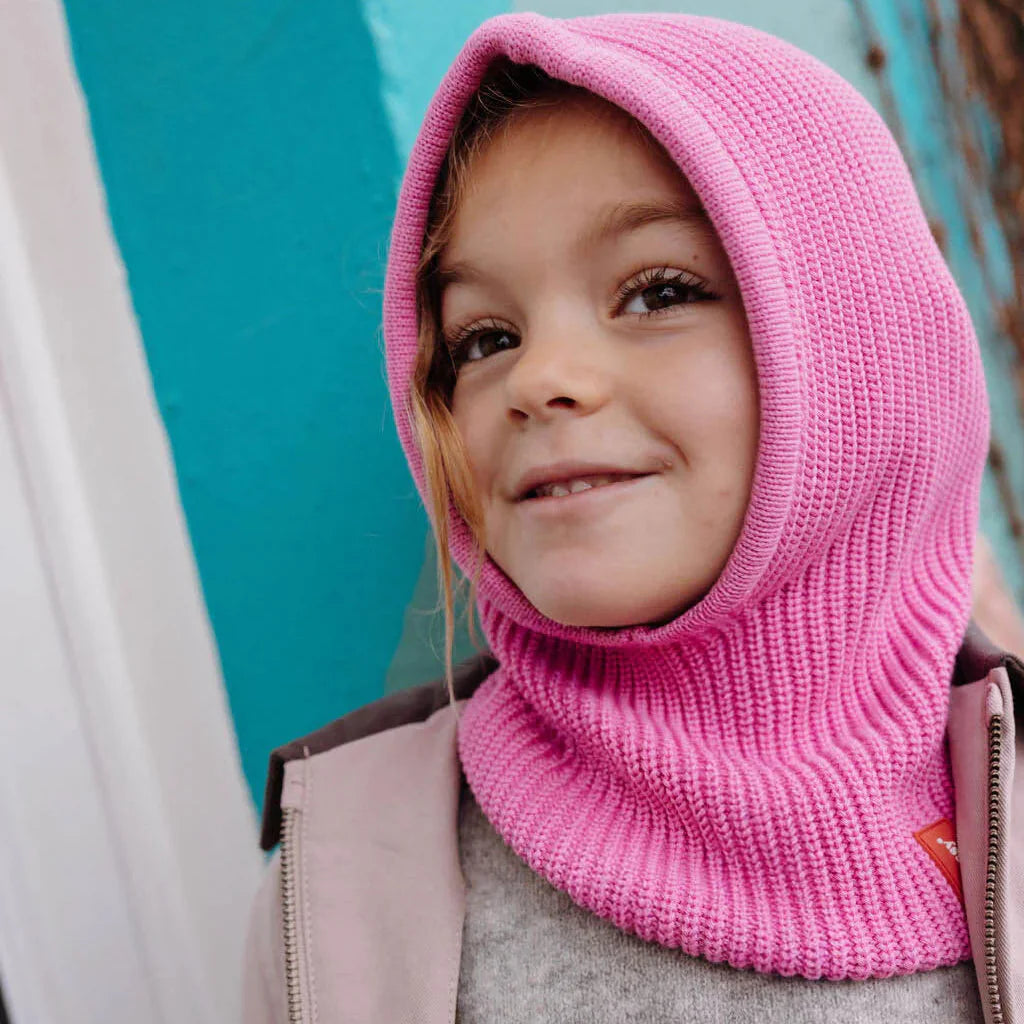 Kind met roze gebreide Hoody Lila van Hello Hossy, die hoofd en hals bedekt.