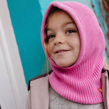 Kind met roze gebreide Hoody Lila van Hello Hossy, die hoofd en hals bedekt.
