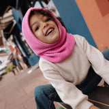 Lachend kind met roze Hoody Lila van Hello Hossy, zittend op een bankje buiten.