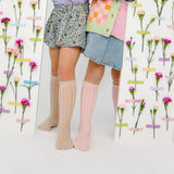 Twee kinderen met beige en roze kniekousen met opengewerkt patroon, tussen panelen met bloemen.