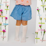 Witte Toni kniekousen met opengewerkt patroon, gedragen met een blauwe short tussen bloemen.