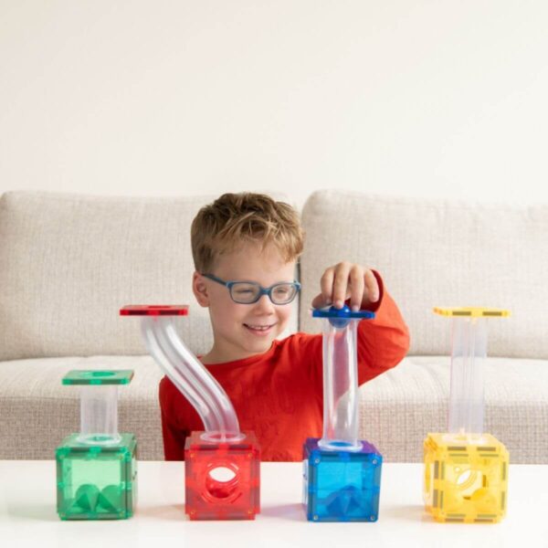 Kind met bril speelt met groene, rode, blauwe en gele knikkerbaanblokken met doorzichtige buizen