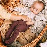 Baby met een paarsbruine geribde maillot Classic in Blueberry, liggend in een rieten mand.