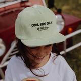 Kind met de lichtgroene Mini Kiwi-pet van Hello Hossy met de tekst ‘Cool kids only’ op de voorkant.