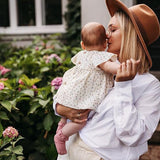 Baby met oudroze Mono Baby sokken met kanten ruches, op de arm van een vrouw in de tuin.