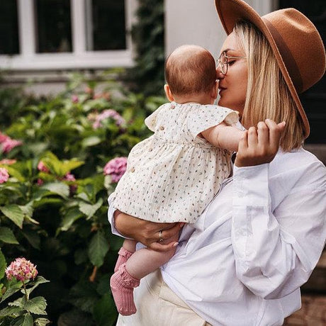 Baby met oudroze Mono Baby sokken met kanten ruches, op de arm van een vrouw in de tuin.