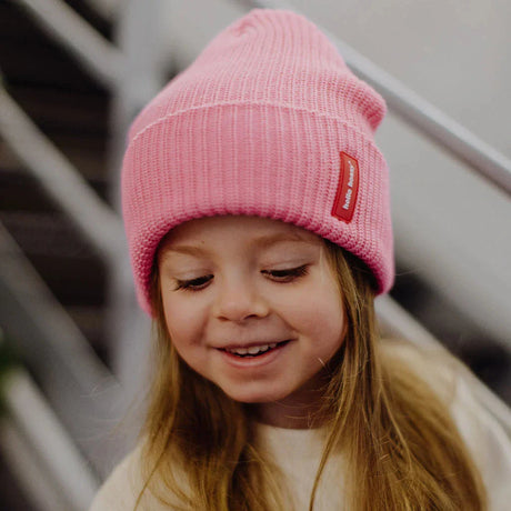 Kind met roze gebreide Flow Pink muts van Hello Hossy, met omgeslagen rand en rood label.