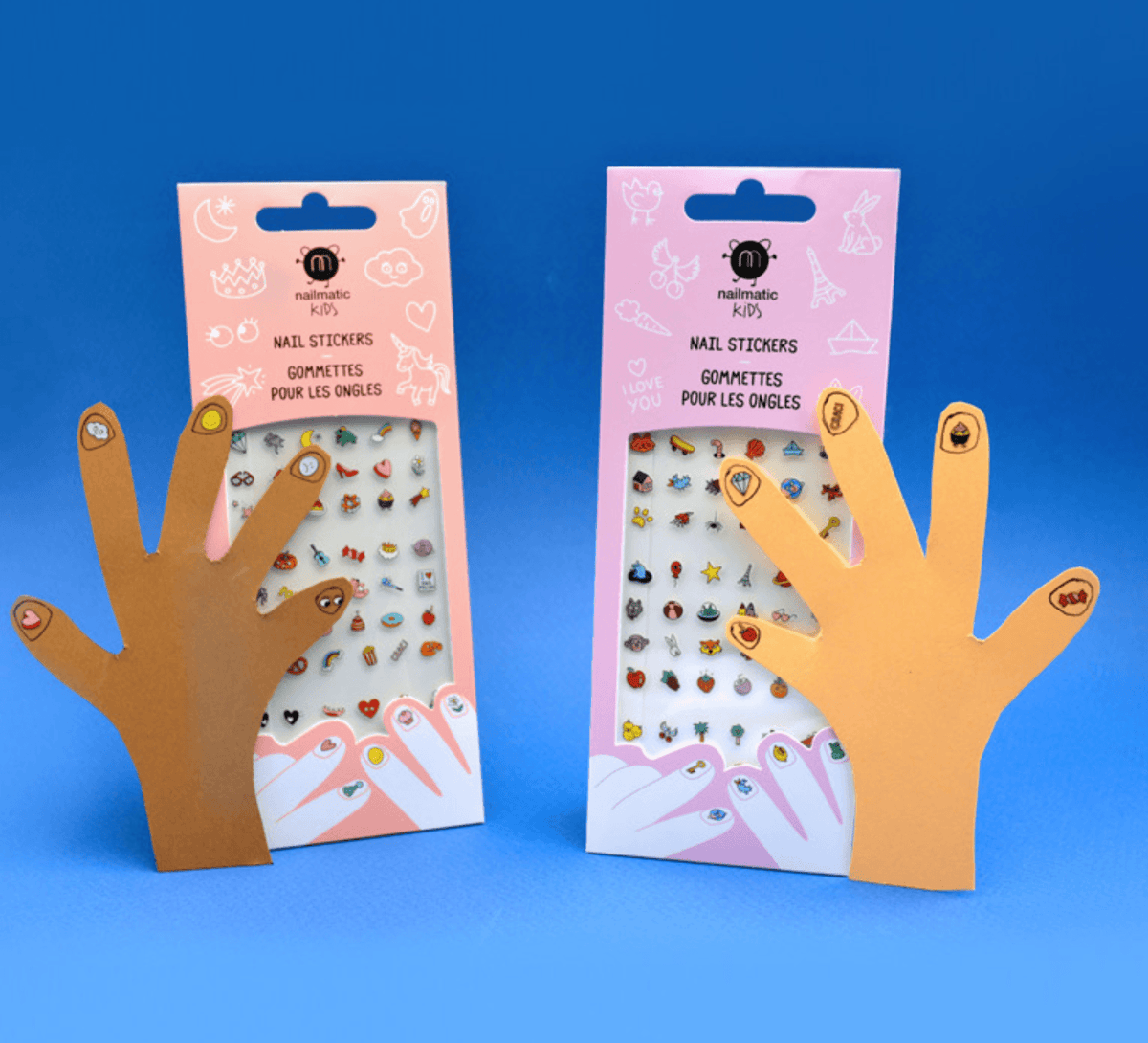 Twee verpakkingen nagelstickers met papieren handen met versierde nagels tegen een blauwe achtergrond.